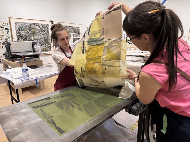 Printer Sarah Madgin, left, and Jillian Ross, right, pull a test print for Wally Dion during the Live Editions/Jillian Ross Print residency at the Remai Modern in Saskatoon, Sask. (photo by Nasibeh Nasibi)